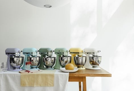 Sześć kolorowych mikserów planetarnych KitchenAid ustawionych w rzędzie na stole